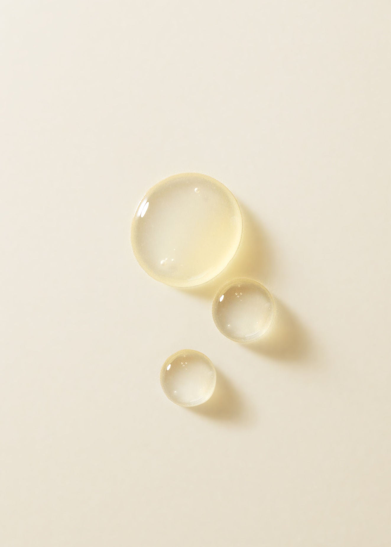 Three drops of oil product on a beige background.