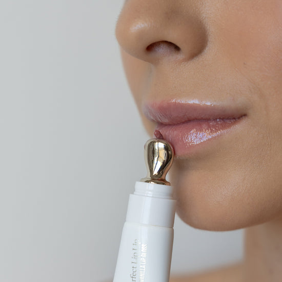 Close-up of a person using a white beauty device with gold tip on their lips against a neutral background