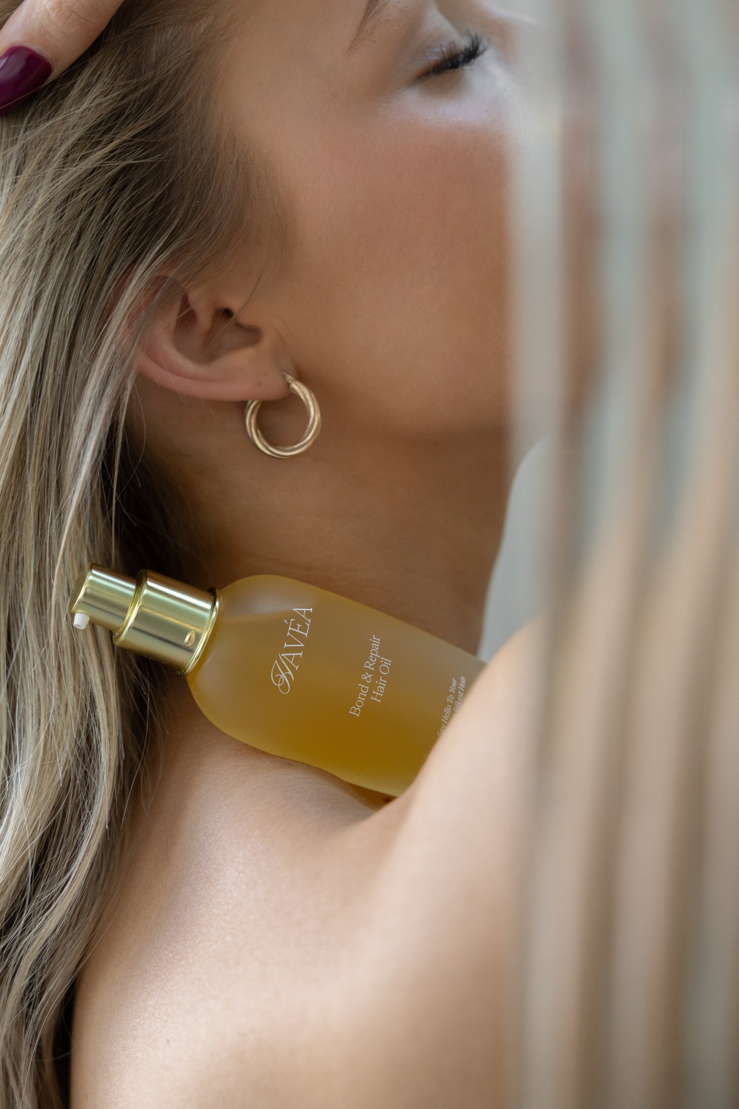 side profile of face of woman with blonde hair and gold hoop earrings. Havea Bond and Repair oil resting on her shoulder.